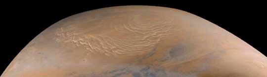 Isbre ved nordpolen på Mars. Isen består av både frosset vann og frosset CO2. Sandstormer blåser det rødlige Mars-støvet ut på isen, som får en rosalignende farge. Til høyre på bildet vises noen blåhvite skyer.